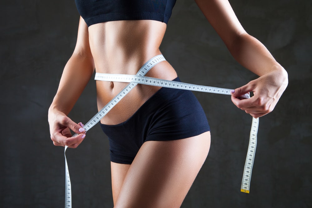 Athletic slim woman measuring her waist by measure tape