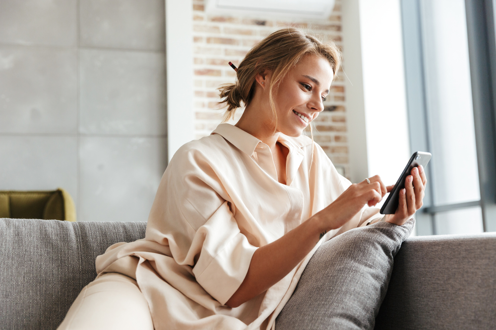 Happy woman in pajamas smiling and using cellphone